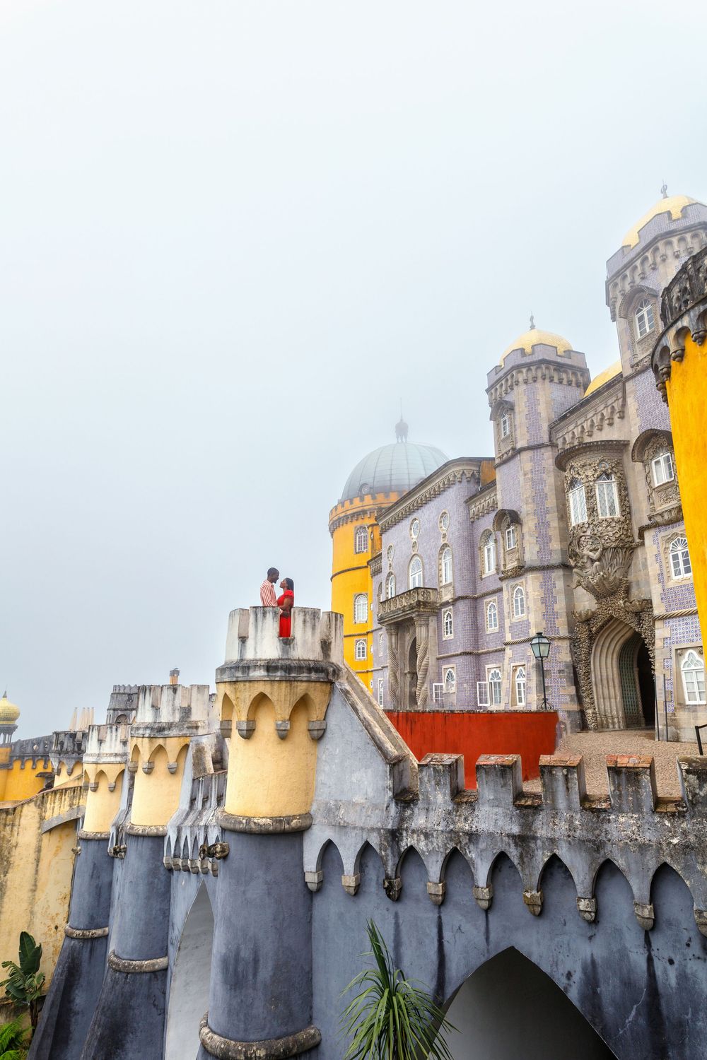 Iconic views of Pena Palace's colorful towers and ramparts in Sintra, Portugal against a cloudy sky.