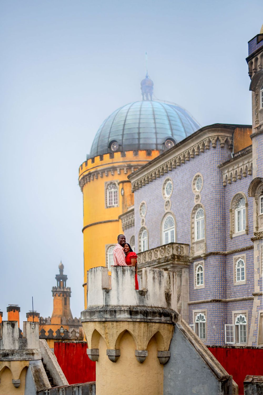 Architectural details of the Pena Palace in Sintra, Portugal showing ornate domes and yellow towers against cloudy sky.