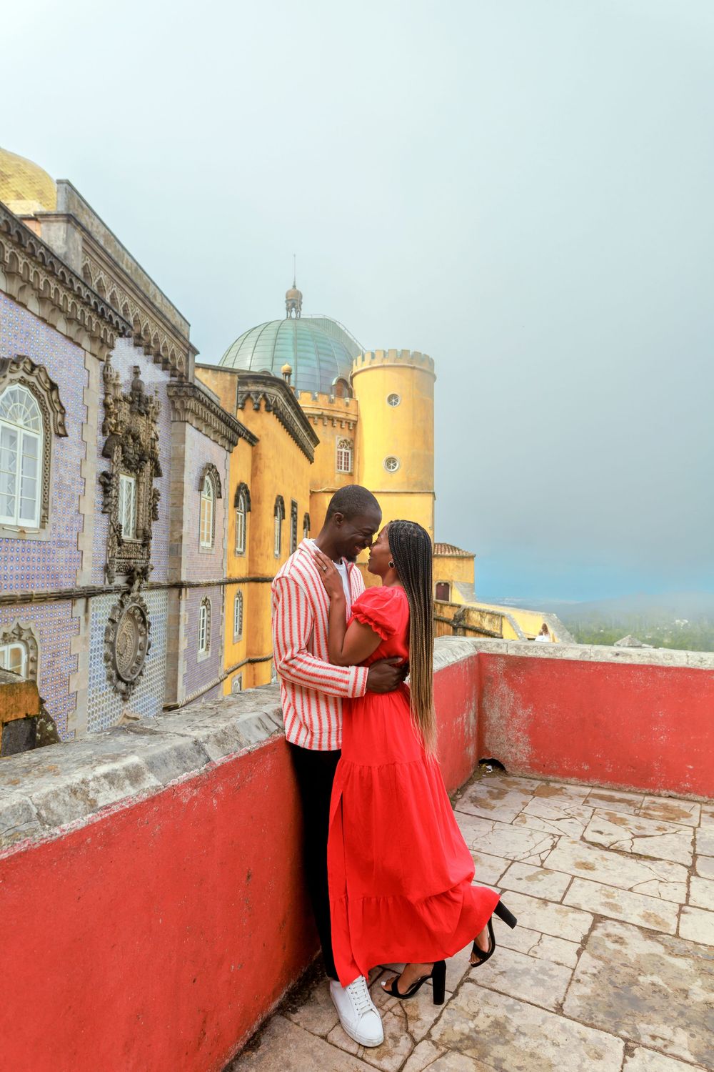 Romantic couple embraces at the colorful Pena Palace in Sintra Portugal with its iconic domed architecture and yellow tower.