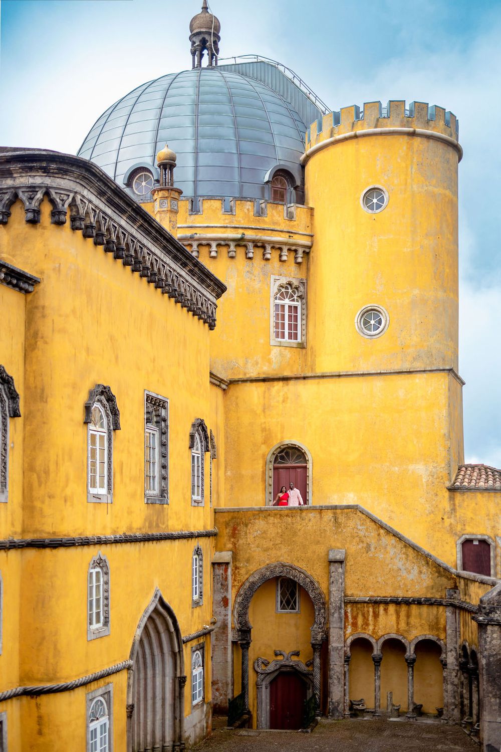 Yellow stone walls and towers of Pena Palace showcase Romanticist architecture with curved arches and ornate details.