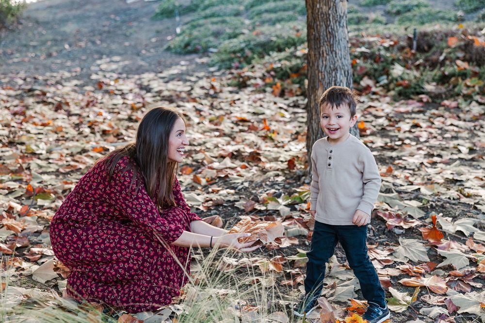 A playful autumn scene with fallen leaves on the ground as two people share a joyful moment outdoors.