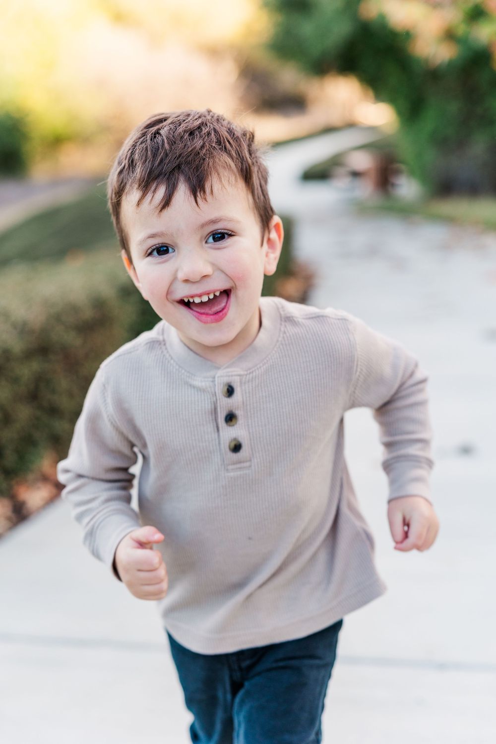 A child in a beige sweater runs and plays outside with a joyful expression.