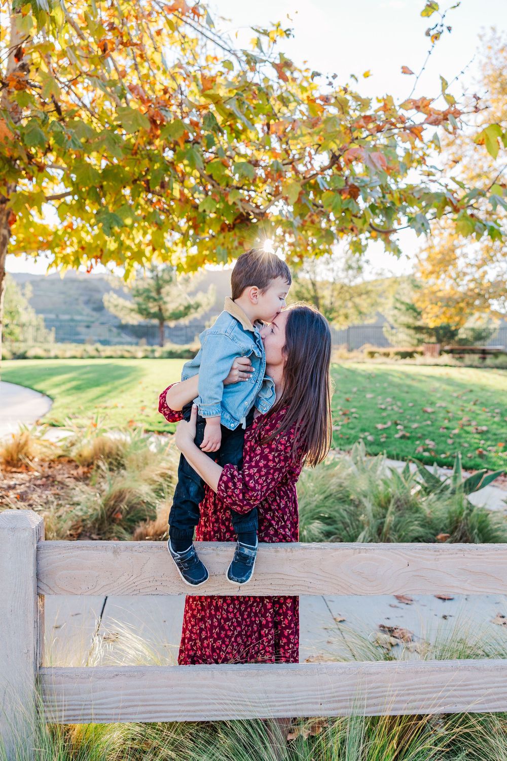 A touching outdoor scene with a family sharing playful moments along a wooden fence during fall.