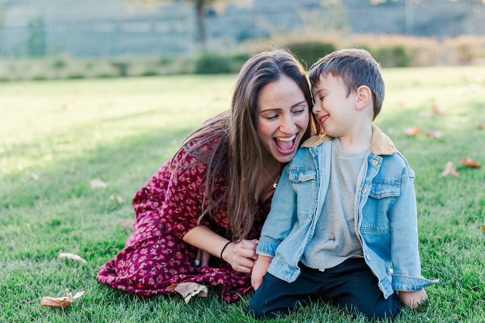 A loving moment is shared between two people sitting together on grassy hillside during golden hour.