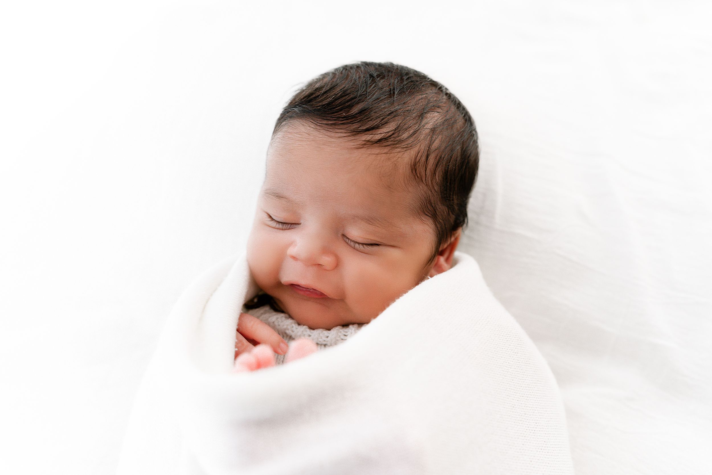 Sleeping newborn baby wrapped in soft white blanket against white background.