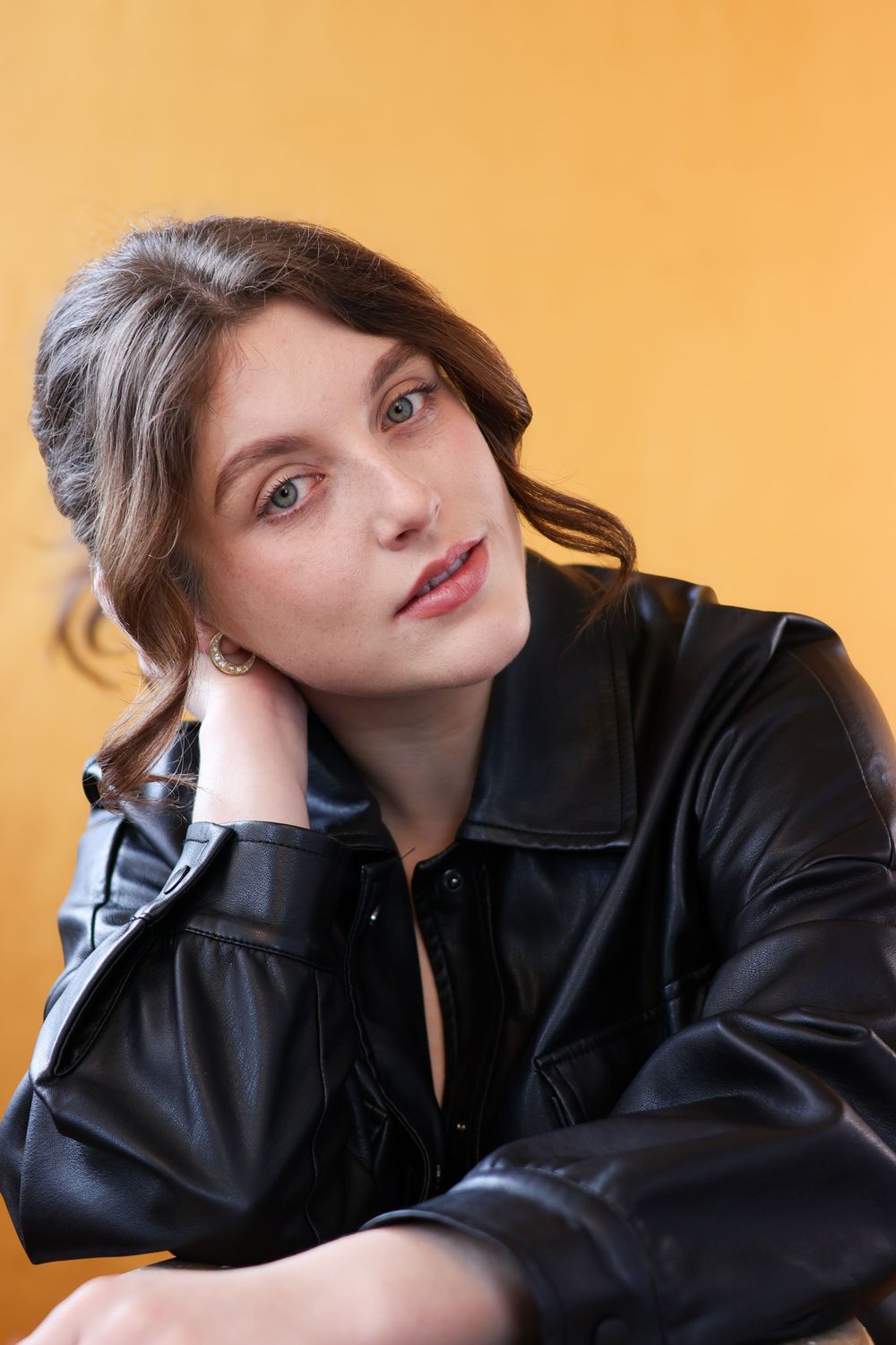 Person in black leather jacket with styled hair against orange background.
