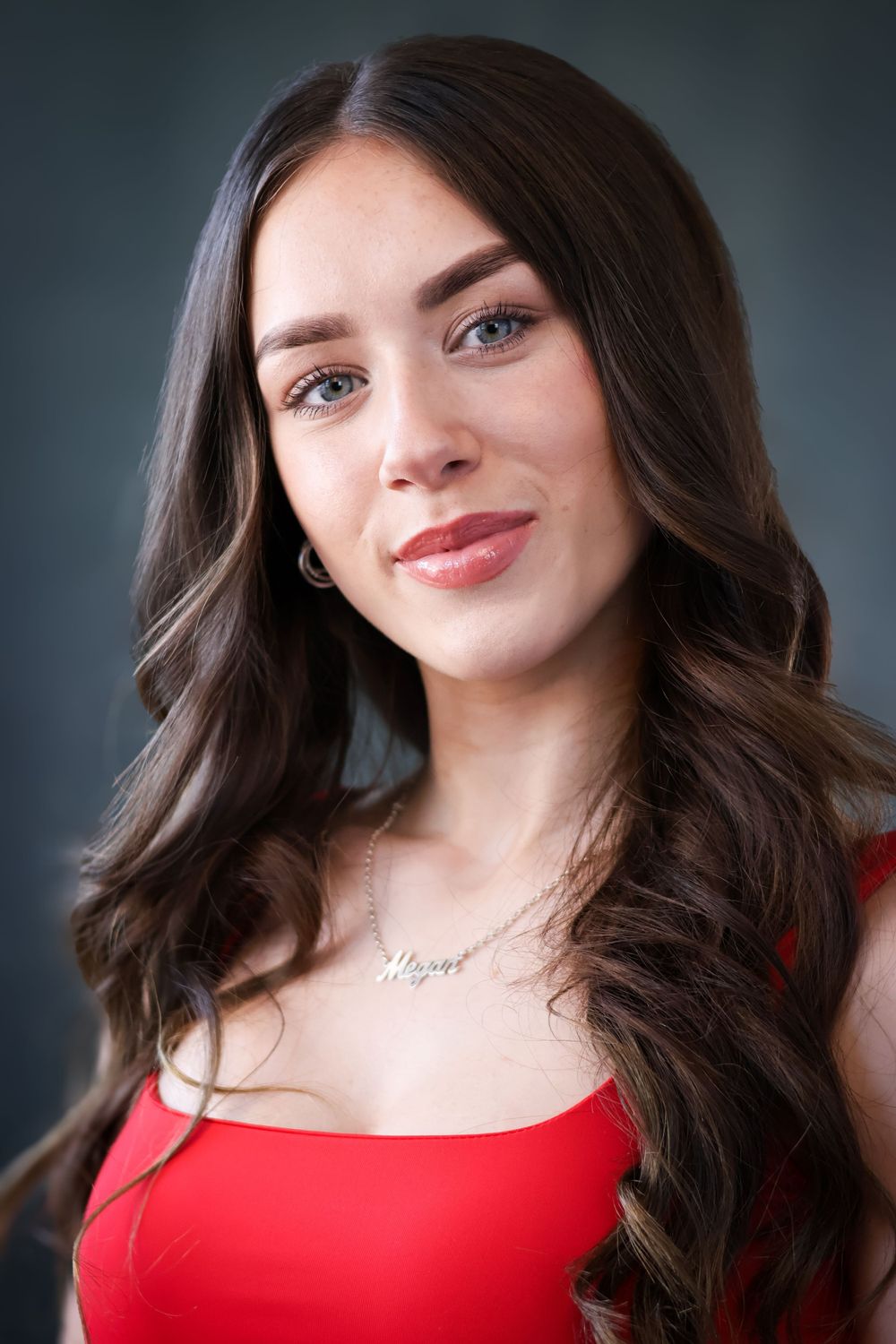 Portrait of smiling woman with long dark wavy hair wearing red top against dark background.
