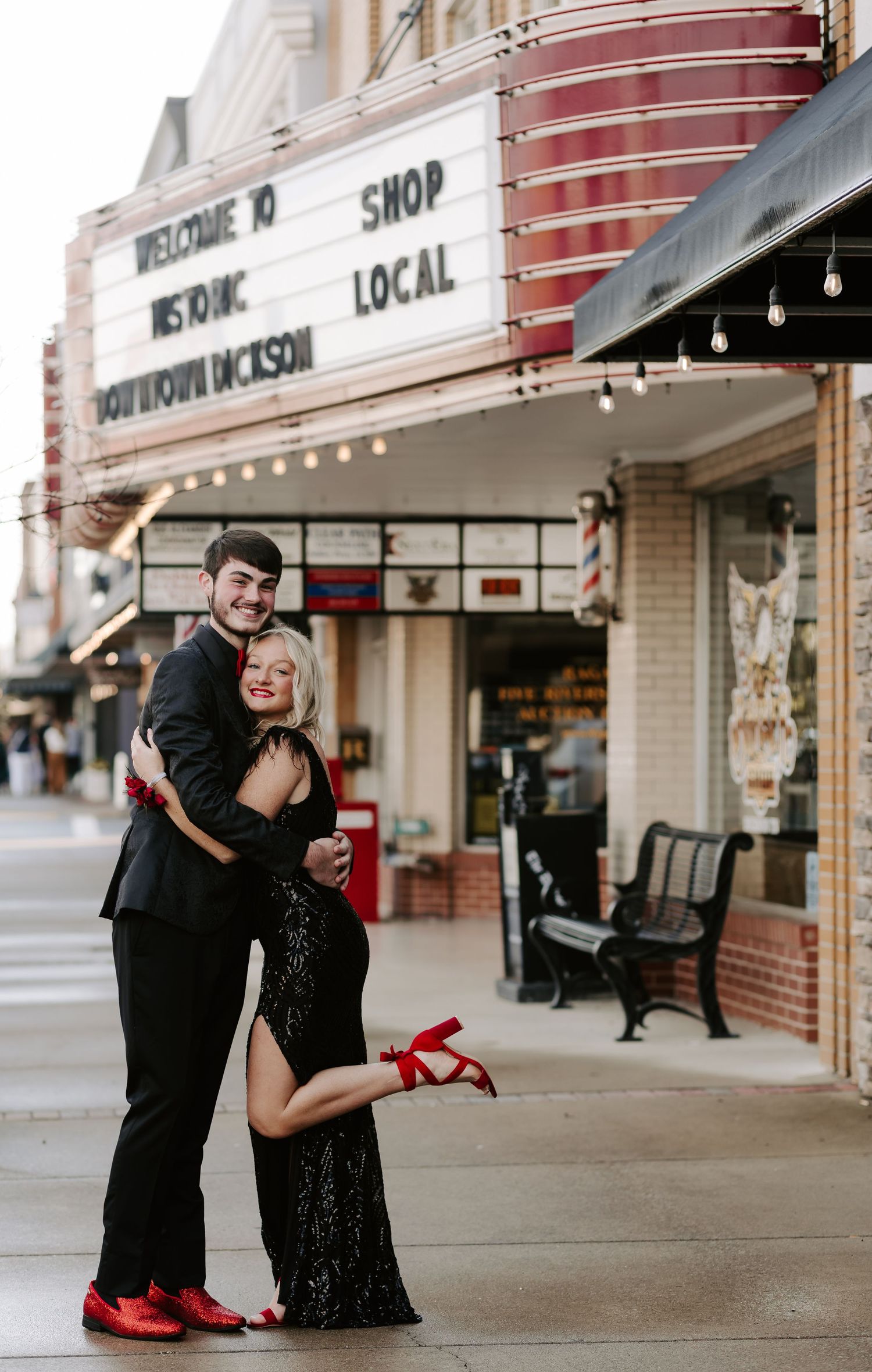 A couple in formal attire shares a joyful moment outside a local shop.