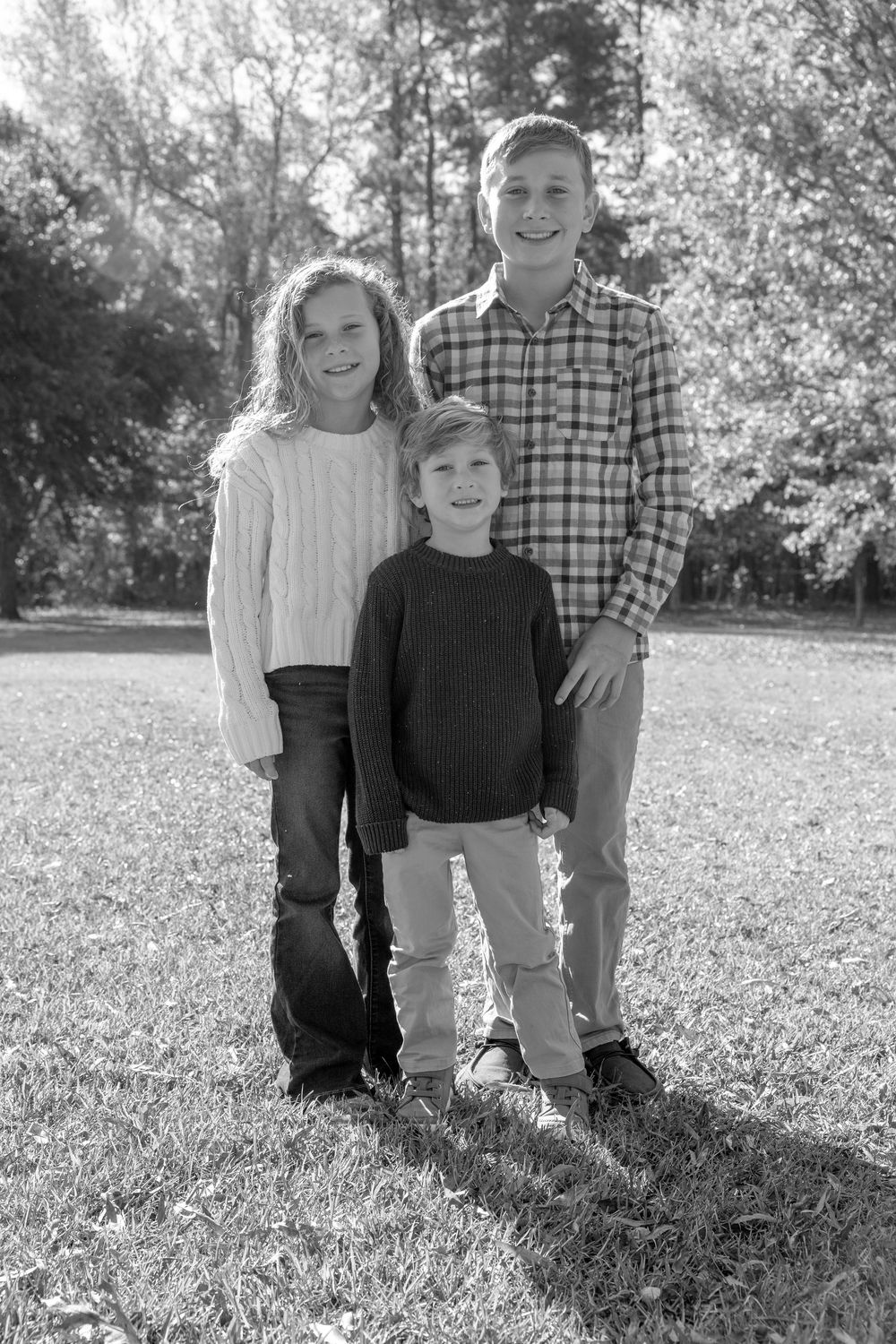 A family group poses together on a grassy hill during an outdoor autumn photo session.