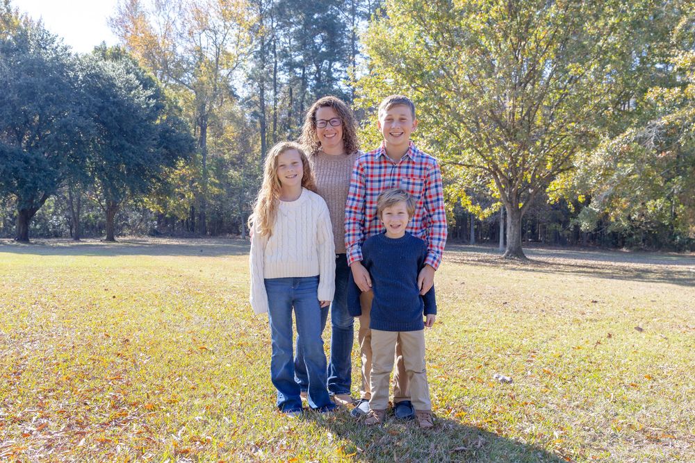 A group poses together on a sunny autumn day with golden leaves and trees in the background.