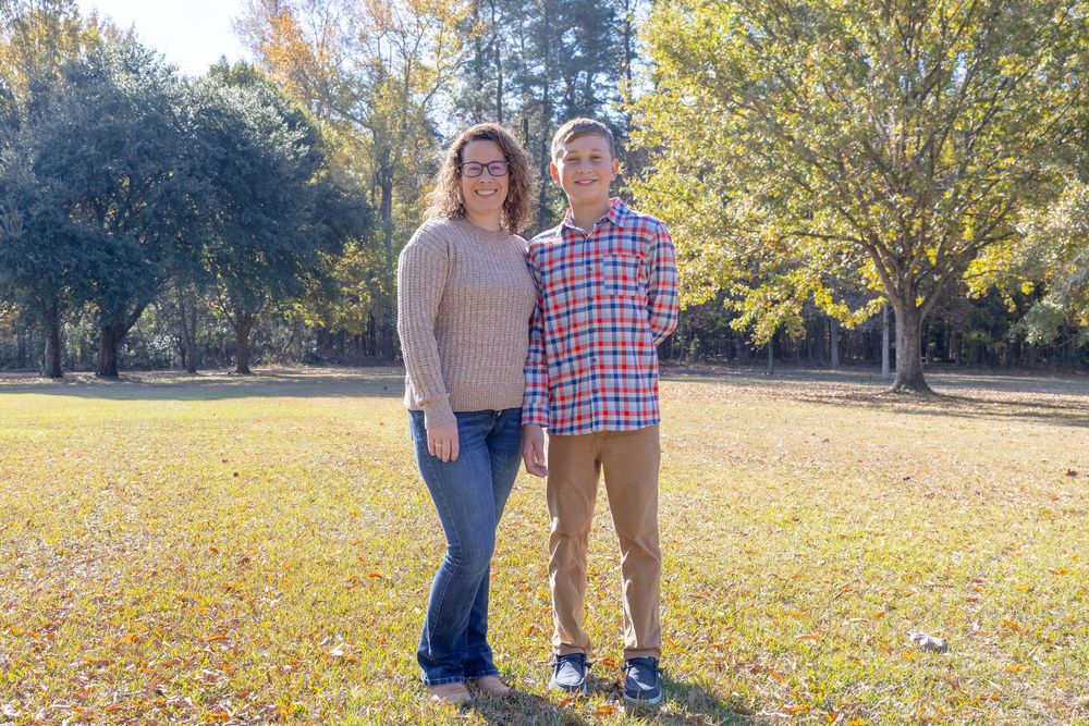 A couple poses together in a scenic autumn park setting with golden fallen leaves scattered on the ground.