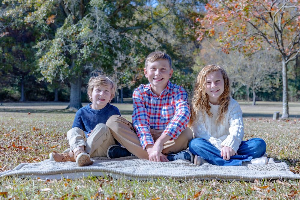 Family lying on blanket in autumn park surrounded by colorful fall leaves during outdoor photo session.