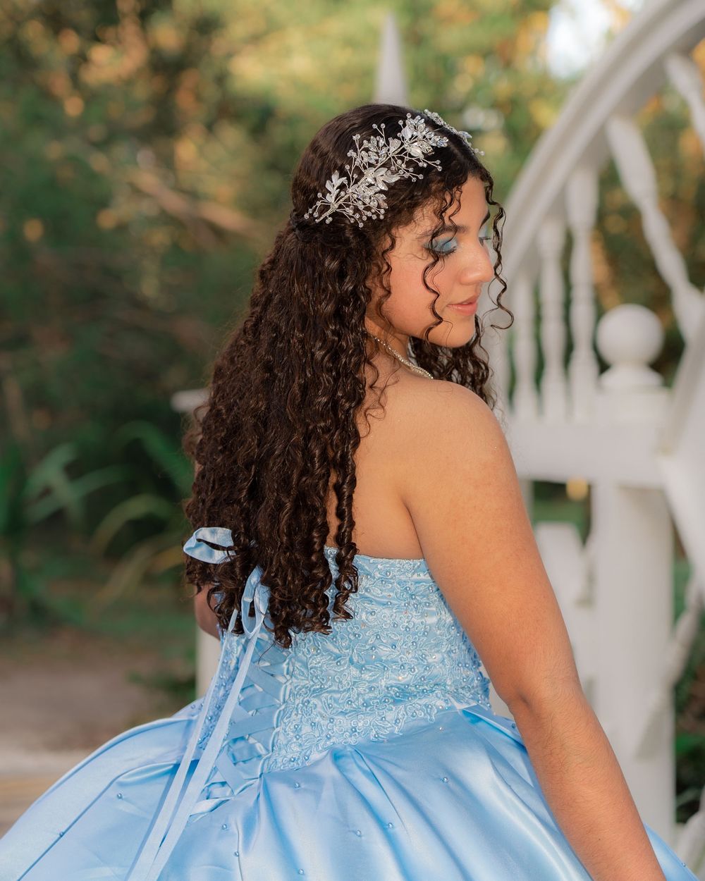 Teen girl in light blue strapless quinceañera gown with silver hair piece and long curly brown hair.