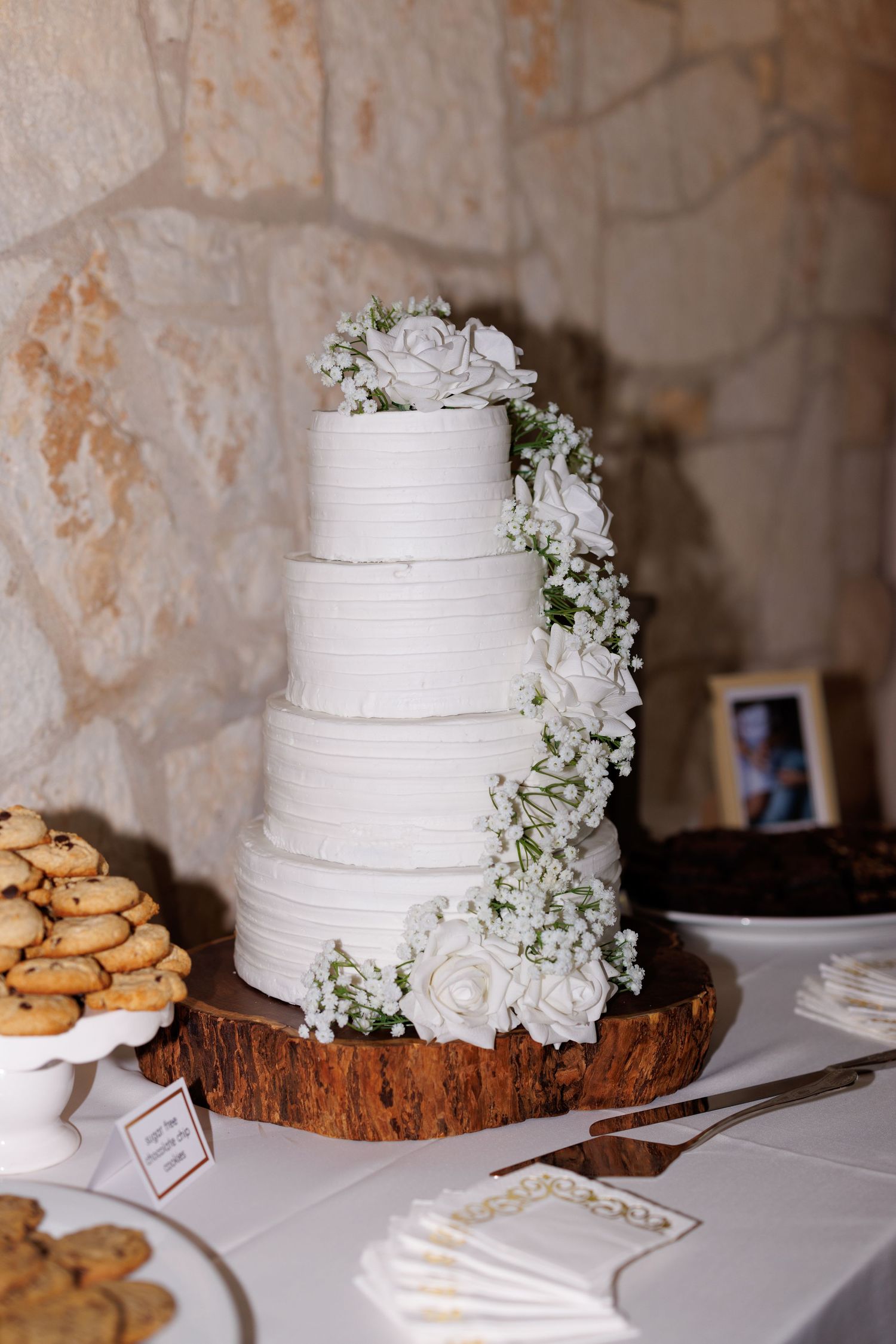 Elegant white tiered wedding cake decorated with flowers on a rustic wooden base.