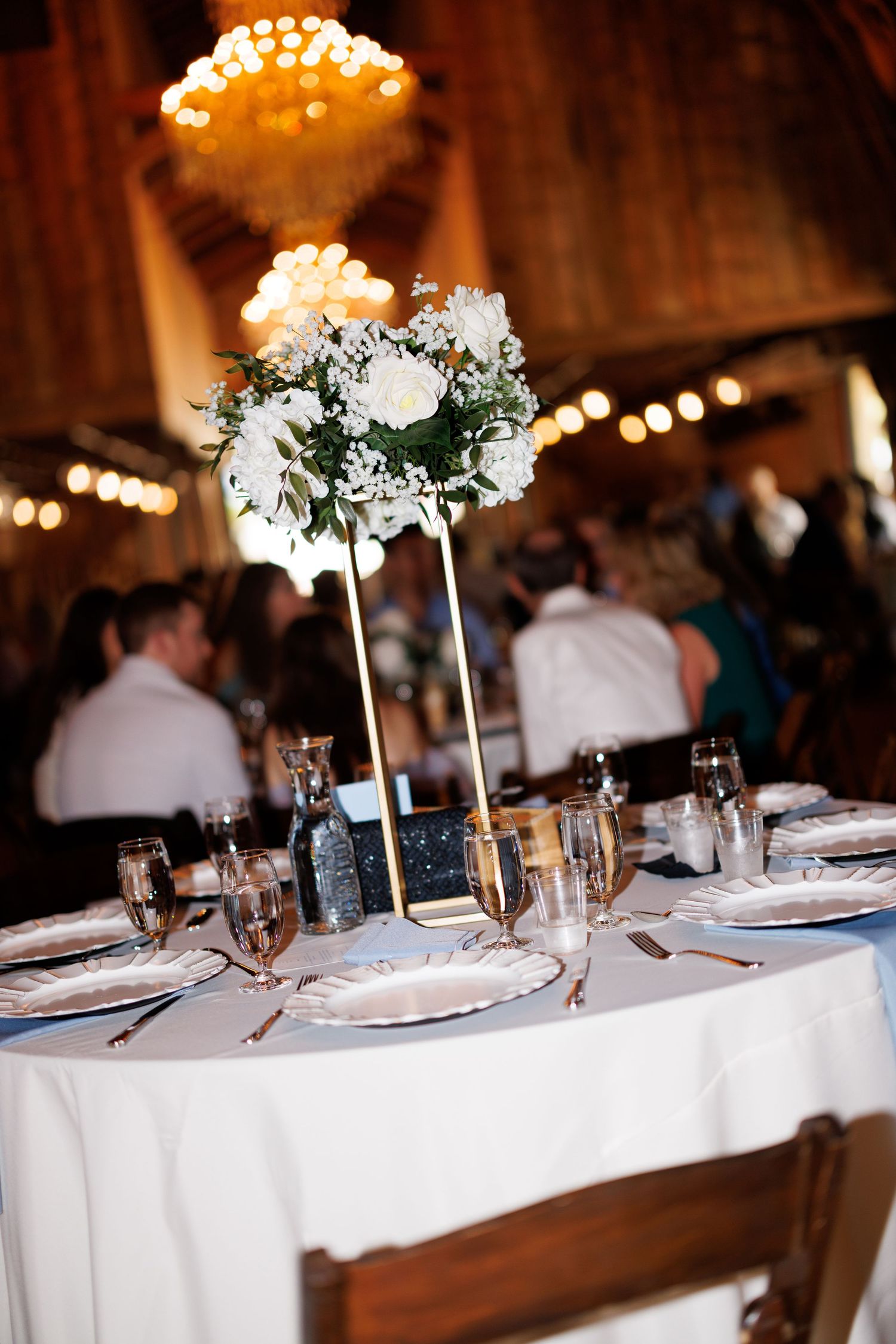Wedding reception table settings with tall floral centerpieces and ambient lighting.