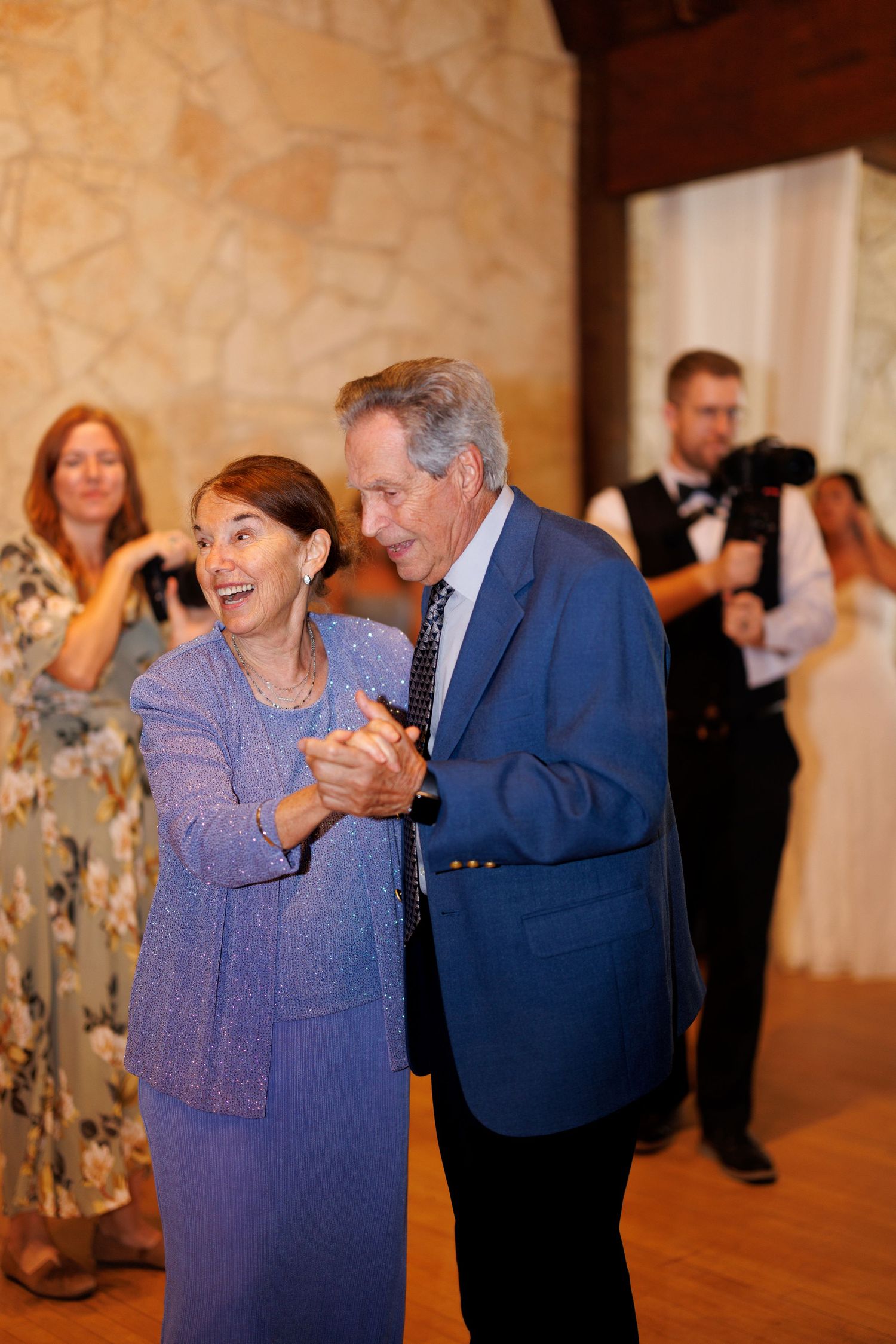 Wedding guests dancing and celebrating in formal attire at an indoor reception.