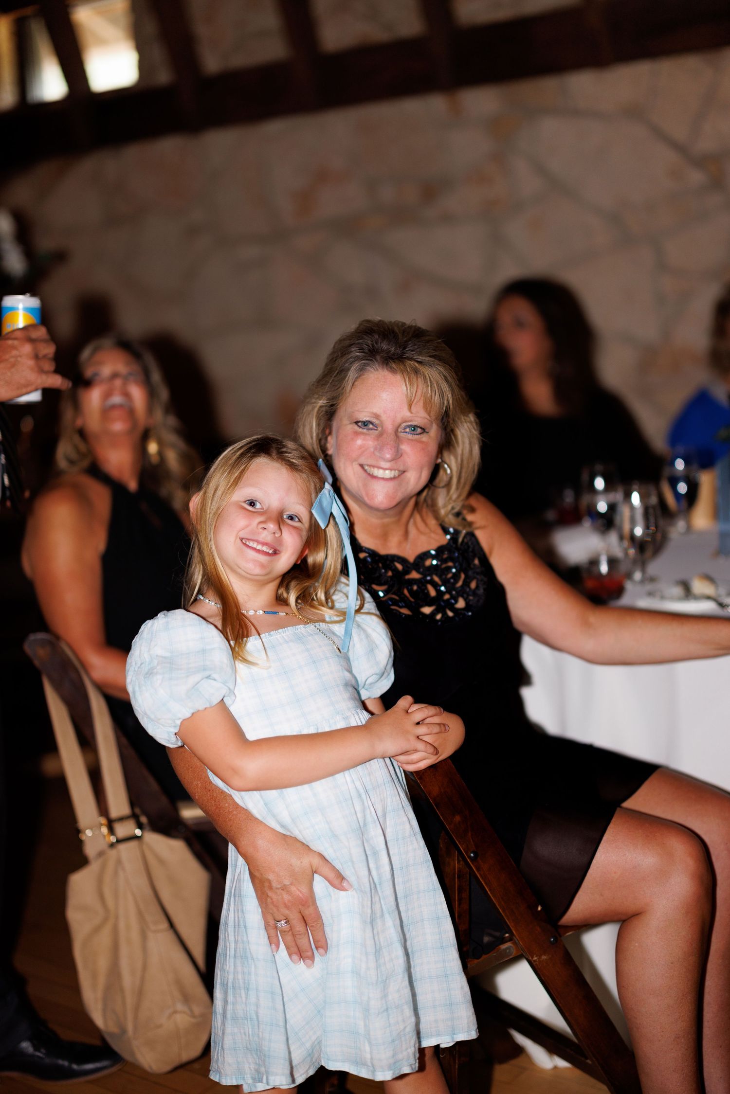A young girl in a white dress shares a tender moment with an adult at a festive gathering.