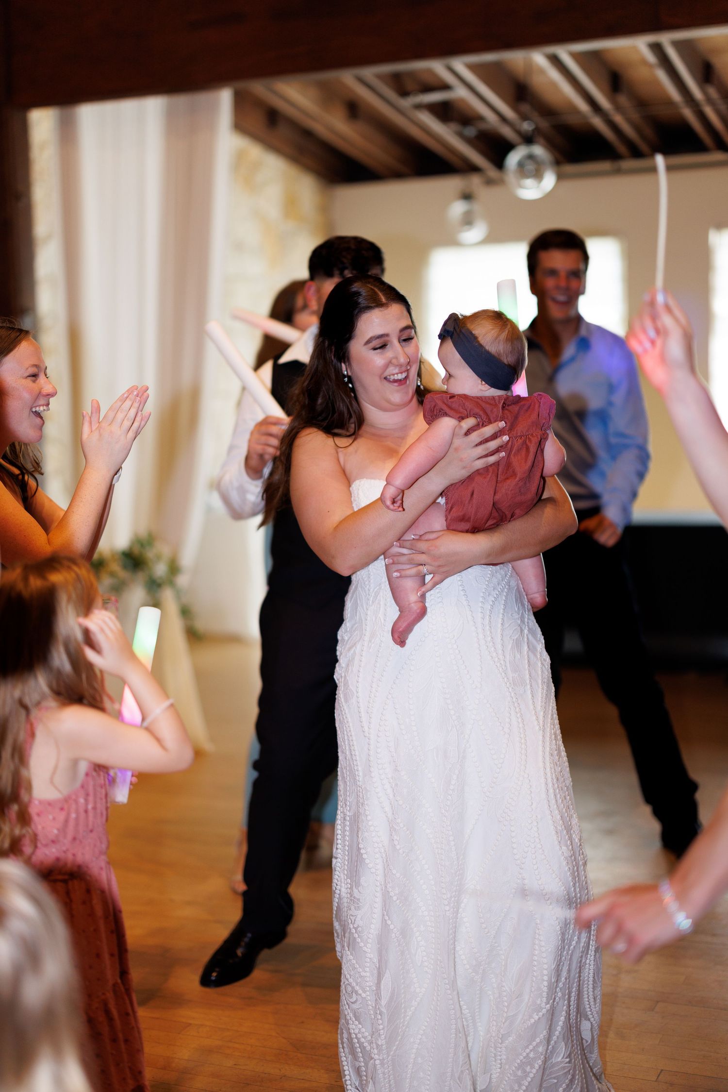 A bride in white dress dances while holding a baby during a wedding reception.