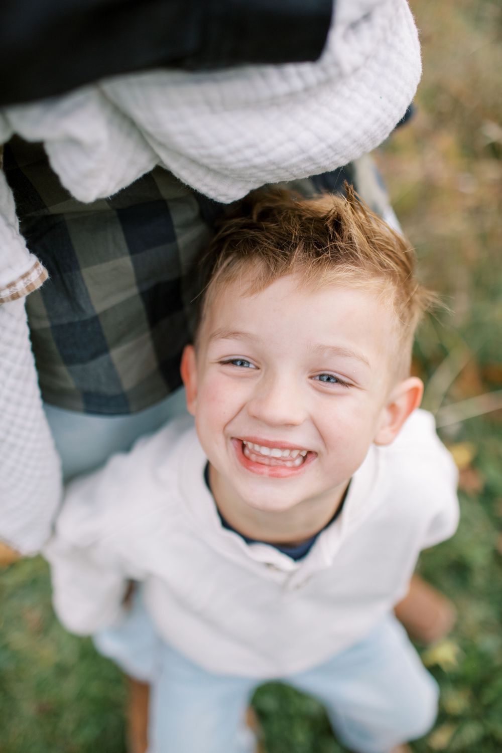 A young child wearing a white sweater and plaid shirt smiles while looking up at the camera from different angles.