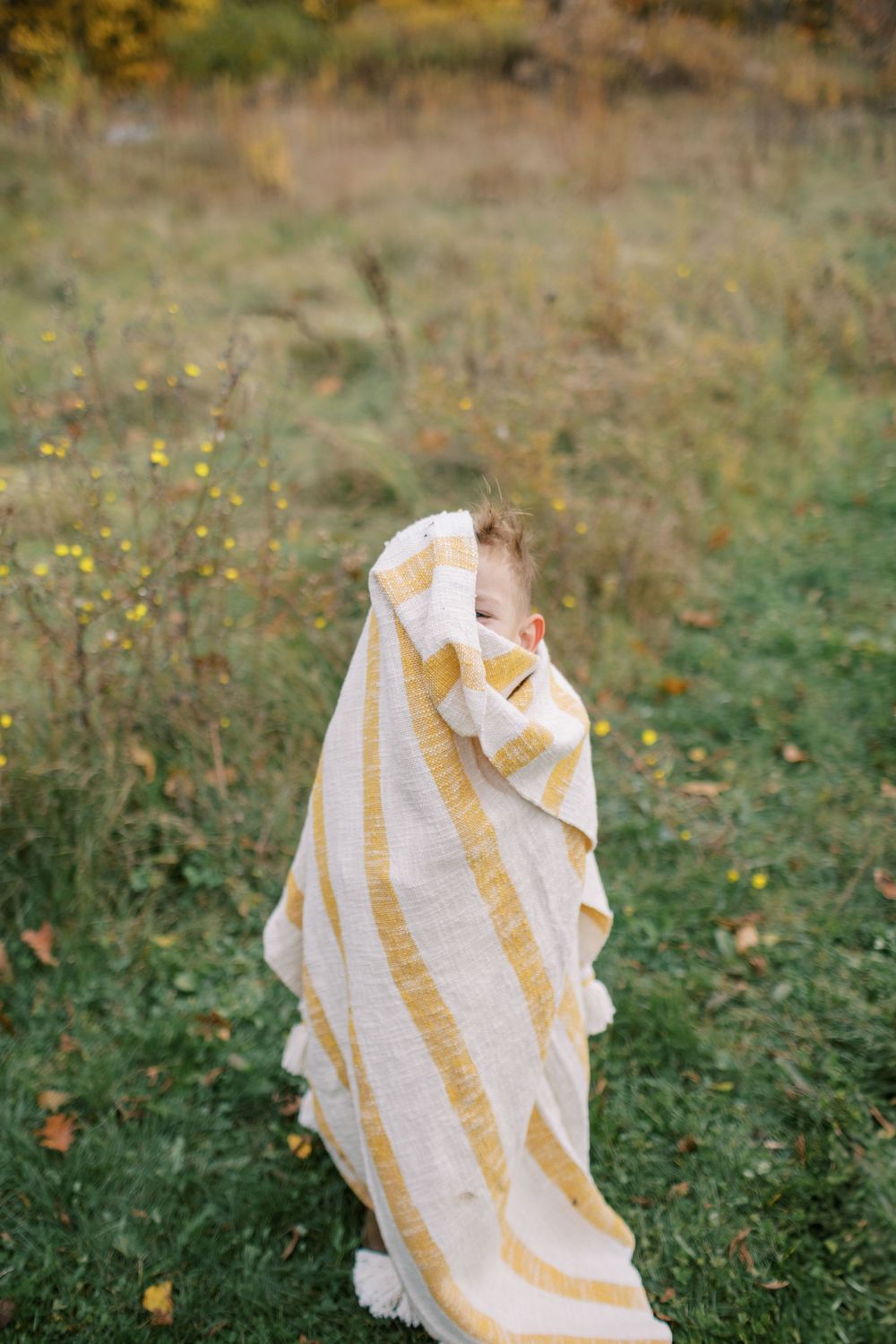 A sequence of photos showing a child wrapped in a white and yellow striped blanket playing on grass with autumn leaves.