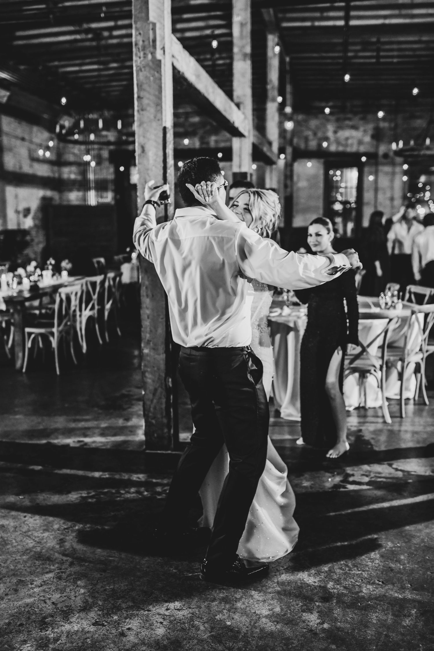Editorial direct-flash shot of the couple mid-dance against exposed brick and warehouse beams.