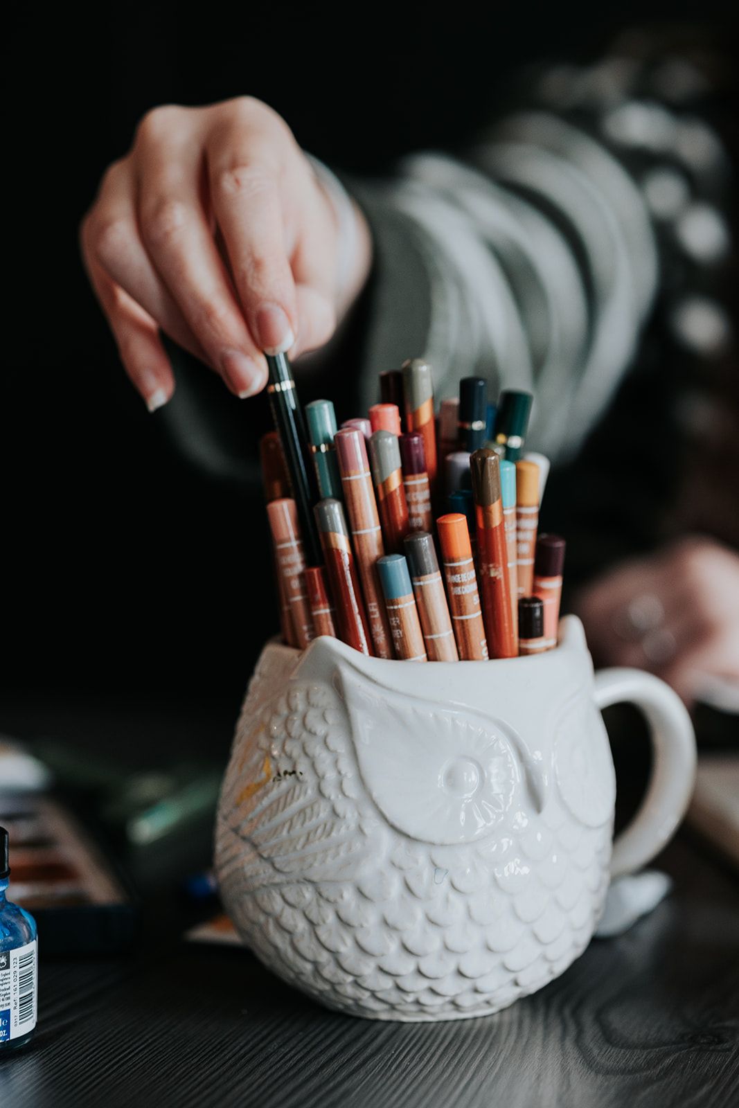 A white ceramic owl pencil holder filled with wooden pencils and art supplies shown from different angles.