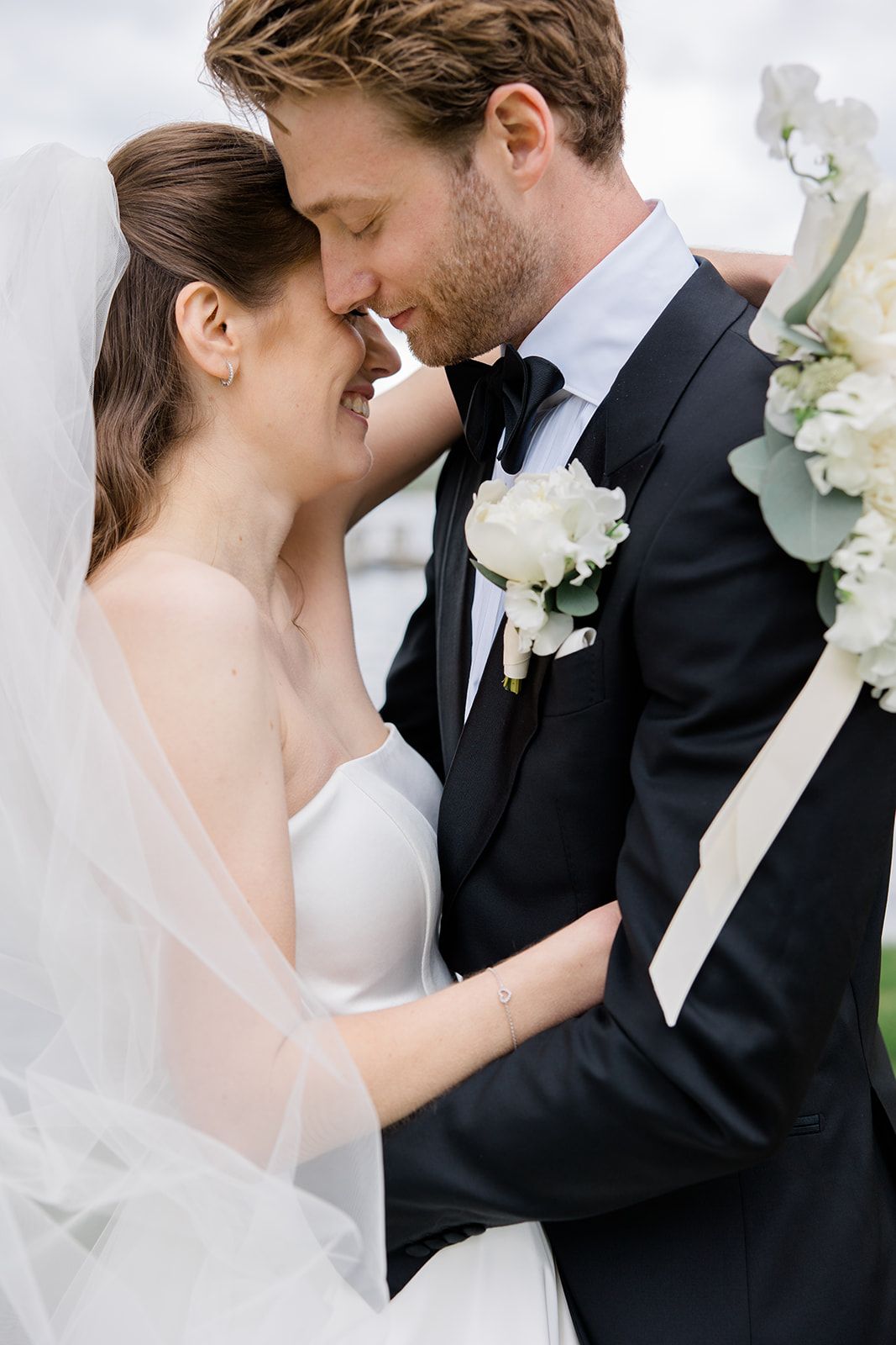 Romantic wedding couple shares an intimate moment in black and white formal attire with white floral accents.