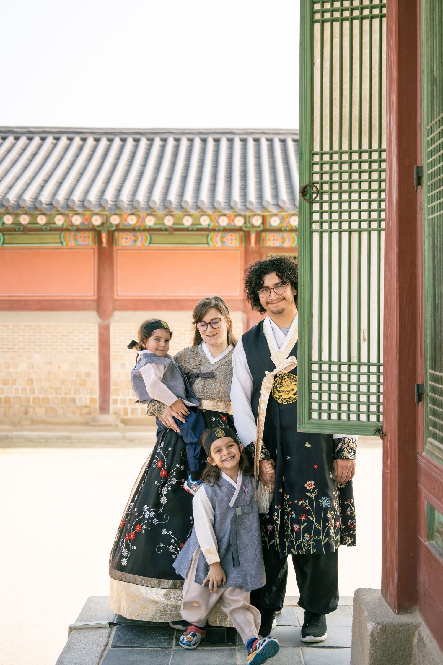 A person in traditional Korean hanbok clothing stands in a courtyard of a historic palace building.