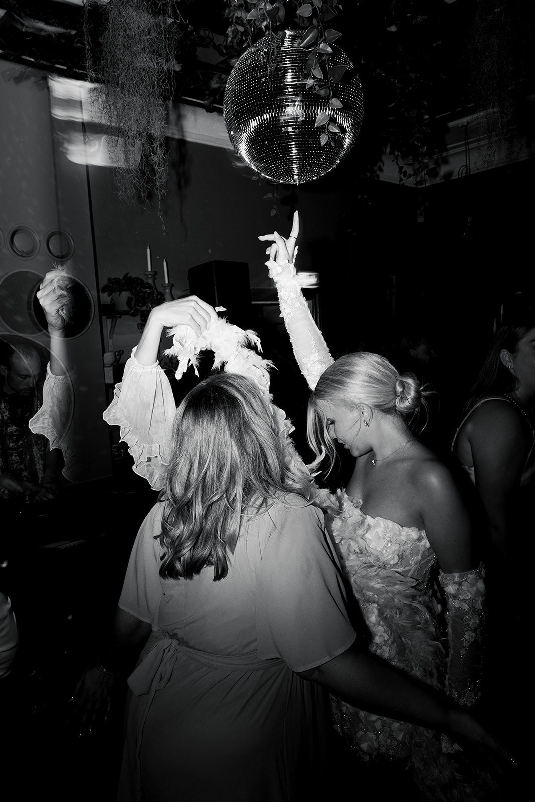 Silhouettes of people dancing in a dark nightclub with a disco ball overhead.