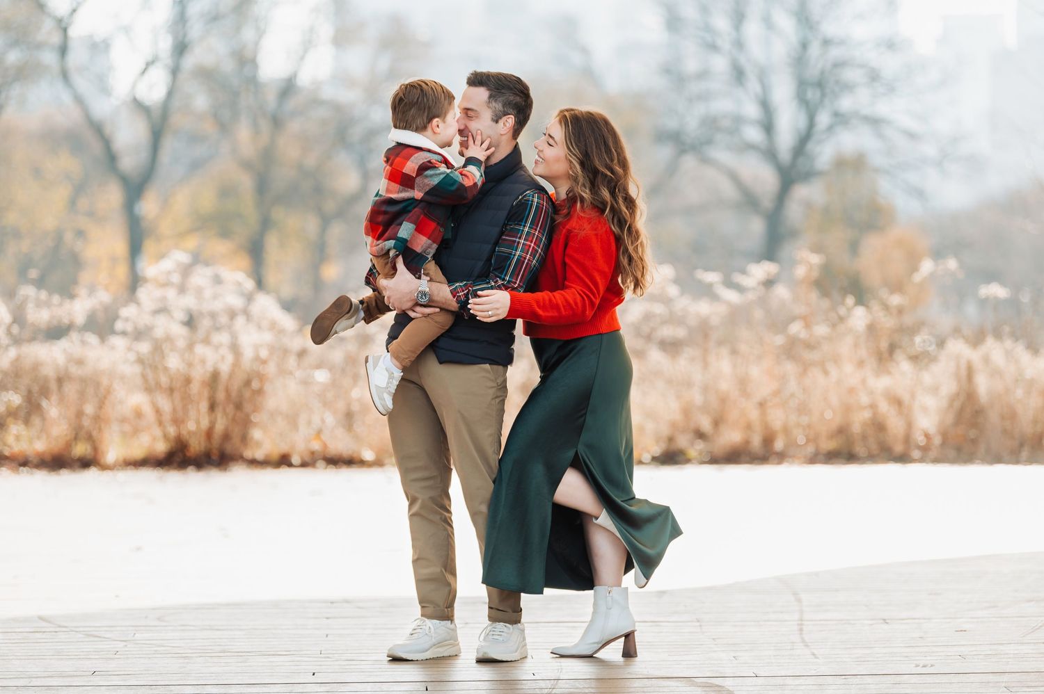 Happy family with young child sharing a kiss outdoors in autumn park setting.