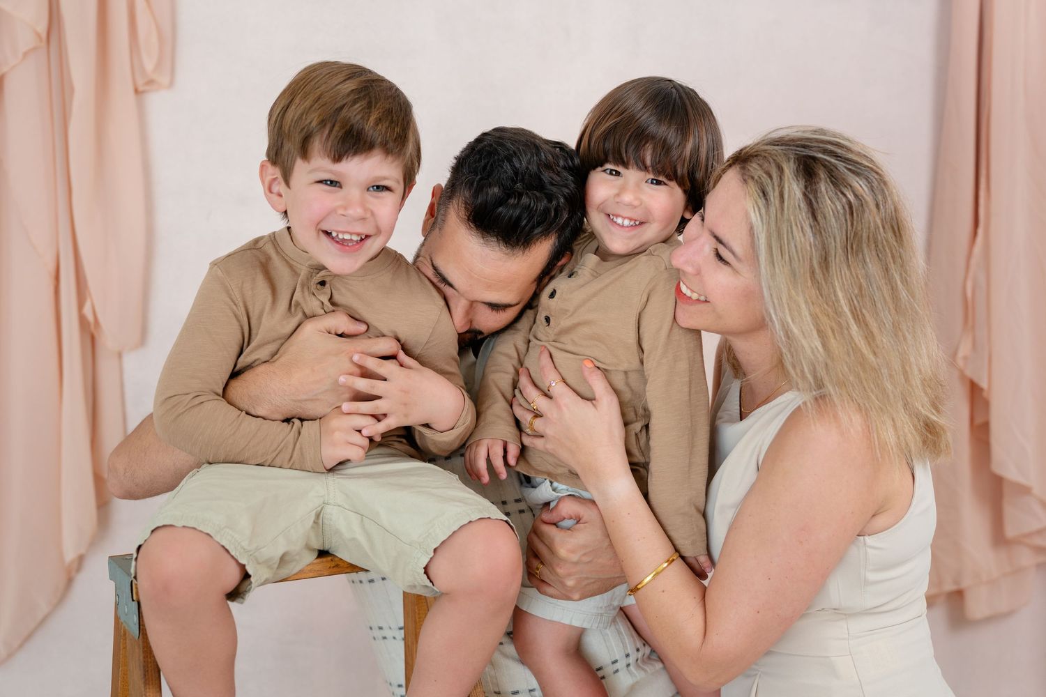Happy family of four posing together in matching beige outfits during a professional photo session.