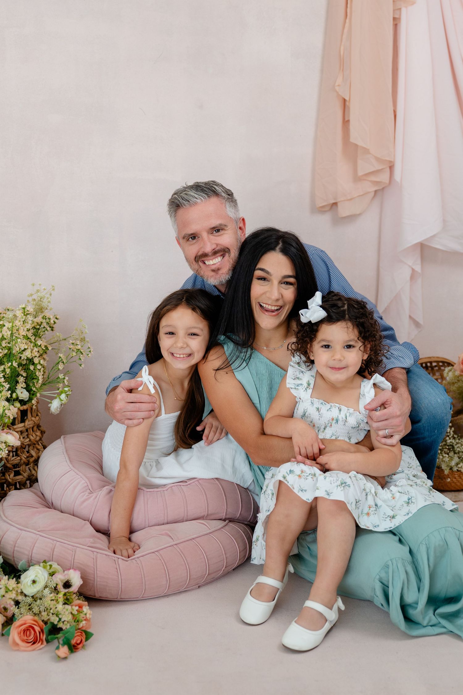 Happy family of four posing together in a bright studio with flowers and pastel decor.