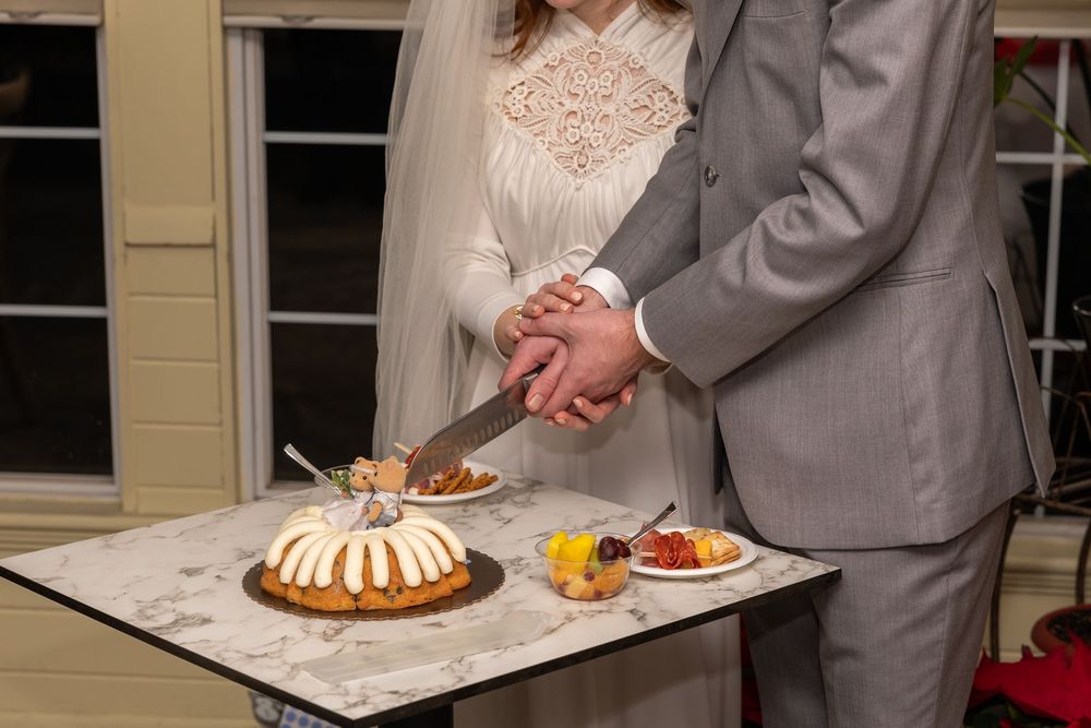 Bride and groom cutting a bundt wedding cake together at a reception table with fresh fruit nearby.