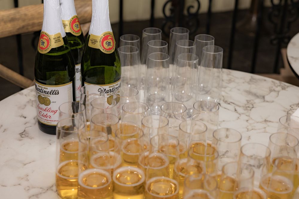 Martinelli's sparkling cider bottles beside rows of filled and empty champagne flutes on a marble table.