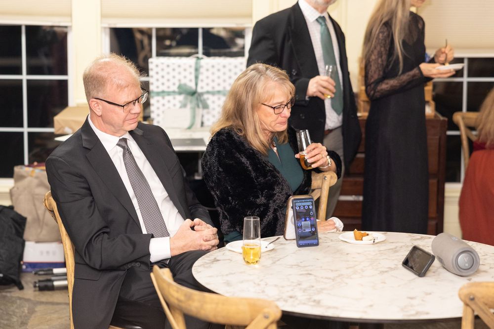 Elegantly dressed couple sitting at a round table during a formal evening event, holding champagne glasses.