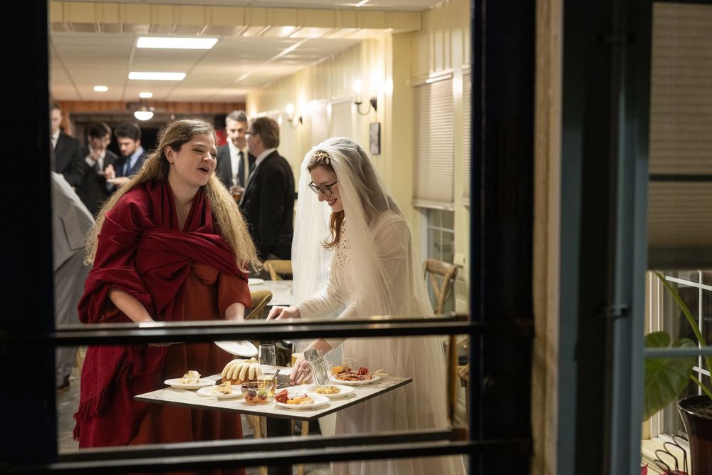 A bride in white veil and woman in red dress share a joyful moment at an elegant indoor wedding reception.
