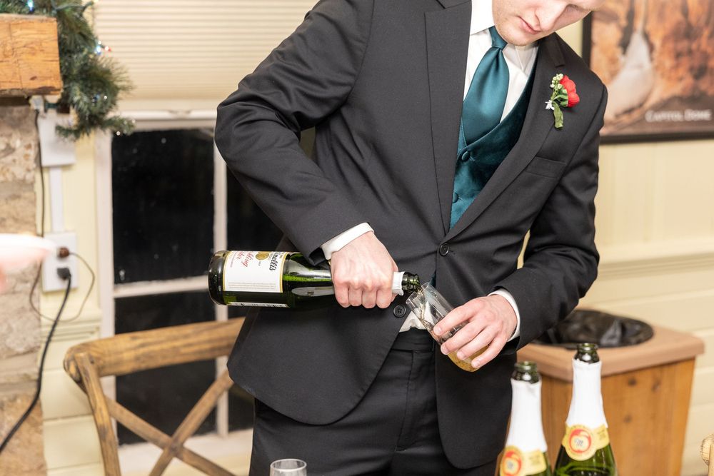 Man in black suit with teal tie pouring champagne at a wedding reception celebration.
