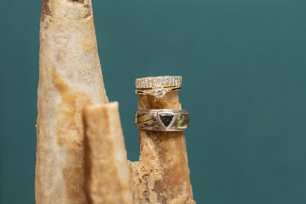 Two stacked silver rings with stone inlays displayed on a natural bone or driftwood prop against teal background.