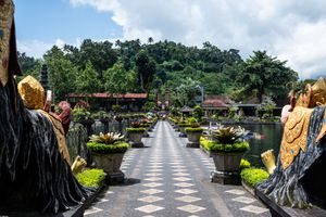 Scenic pathway lined with golden statues and tropical plants leading to a Balinese water palace temple.