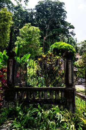 Ancient stone gate surrounded by lush tropical plants and trees in a Balinese garden setting.