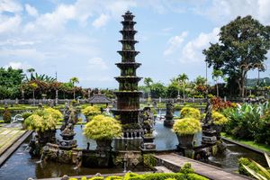 Tiered stone pagoda fountain surrounded by lush gardens and reflecting pools at Tirta Gangga water palace, Bali.