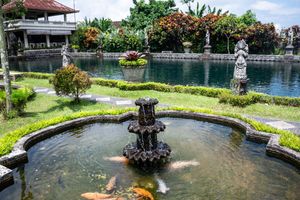 Balinese water palace garden with tiered stone fountain, koi fish, and traditional statues surrounded by lush greenery.