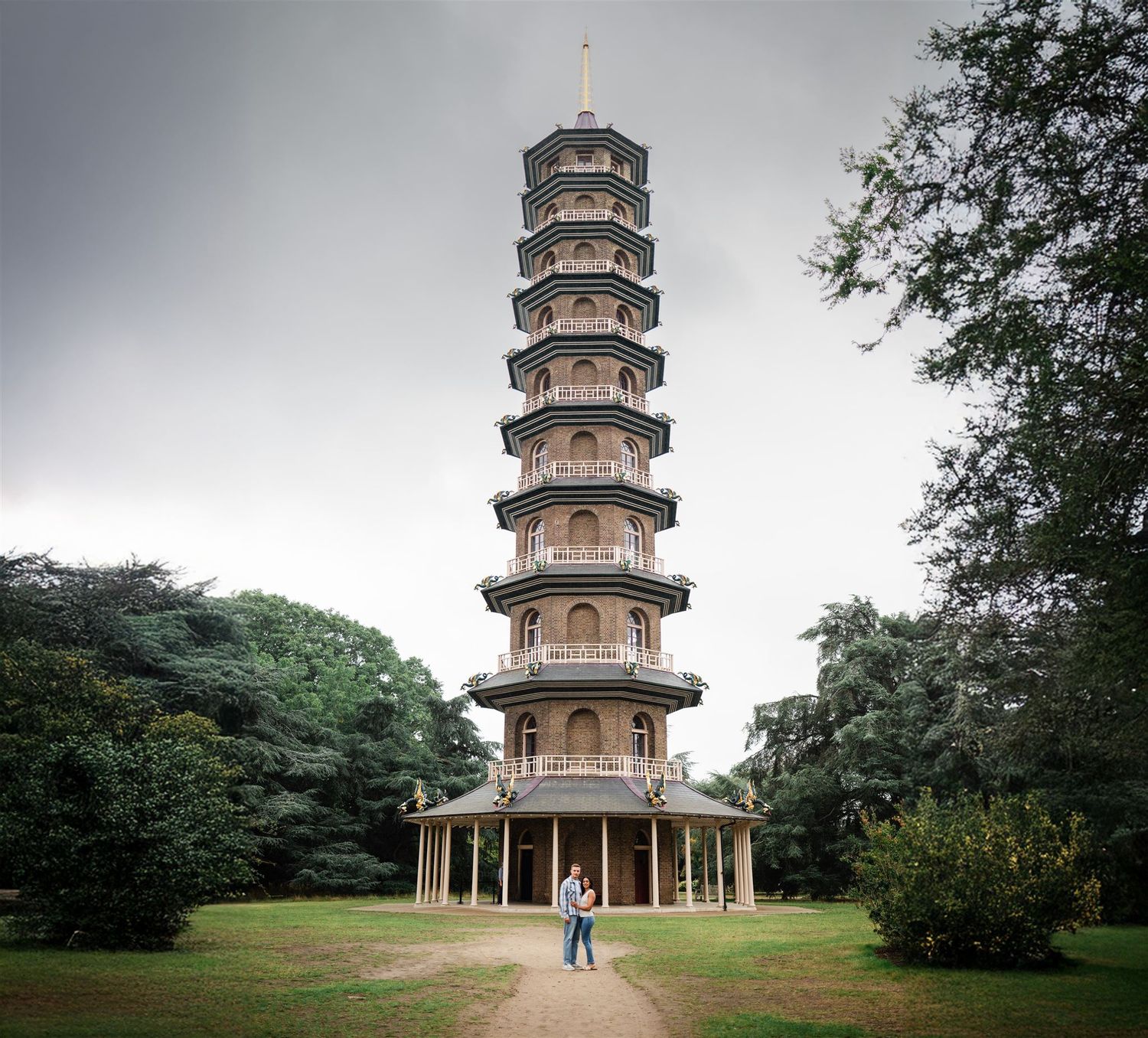 Couple standing in front of the historic Great Pagoda at Kew Gardens, London, surrounded by lush green trees.