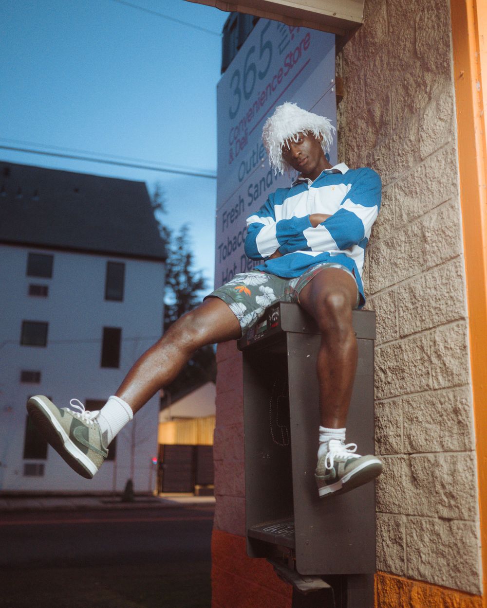 Street fashion photo featuring someone sitting on a ledge wearing a blue and white striped sweater and white sneakers.