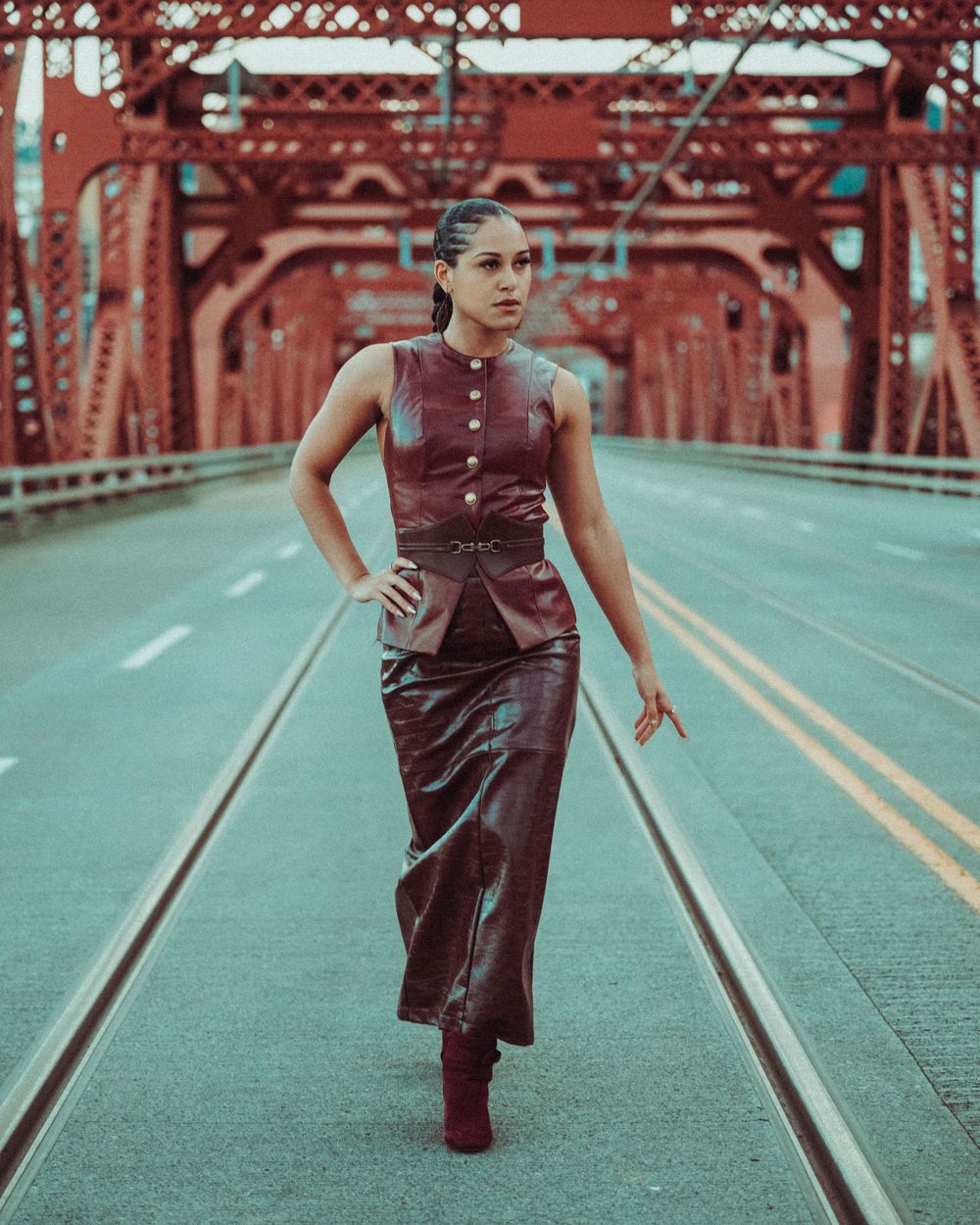 Woman in burgundy leather dress poses confidently on red steel bridge road.