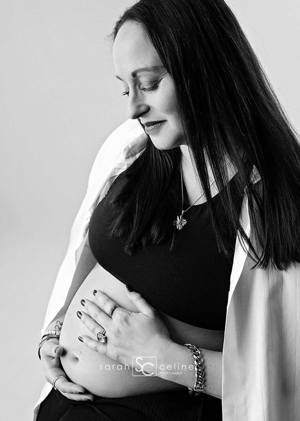 Black and white maternity photo of pregnant woman in black top cradling baby bump with flowing white fabric.