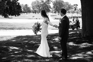 Black and white photo of a bride and groom holding hands outdoors under a tree during their wedding first look.