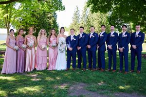 Wedding party posing outdoors, bridesmaids in pink gowns and groomsmen in navy suits flanking bride and groom.