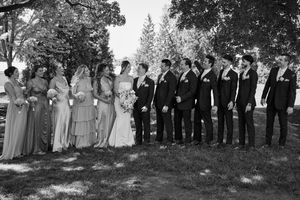 Black and white wedding party photo with bridesmaids and groomsmen lined up outdoors under trees.