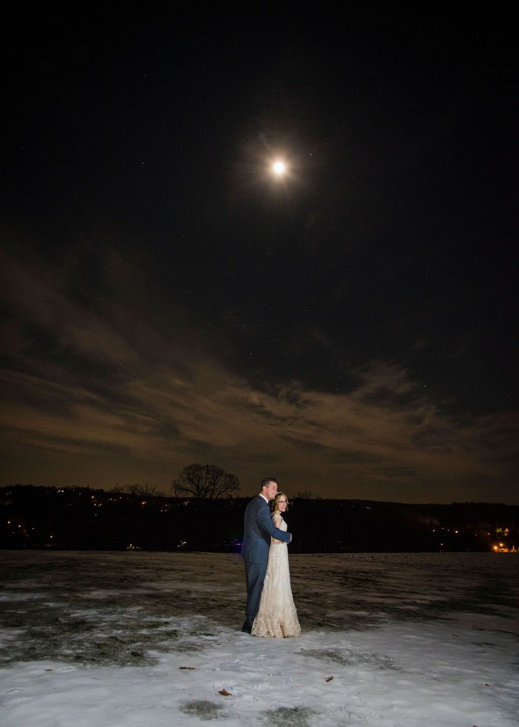 Bride and groom sharing a romantic moment on a swing in a snowy winter landscape with golden sunlight.